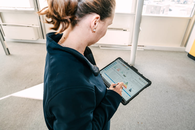 Technicien BTP Diagnostics réalisant un diagnostic de performance énergétique (DPE) sur tablette dans un bâtiment.
