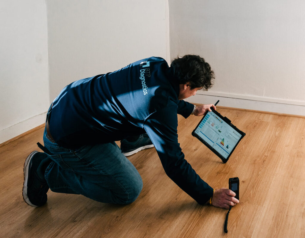 Technicien BTP Diagnostics réalisant un Diagnostic de Performance Énergétique (DPE) à l’aide d’une tablette et d’appareils de mesure sur site.