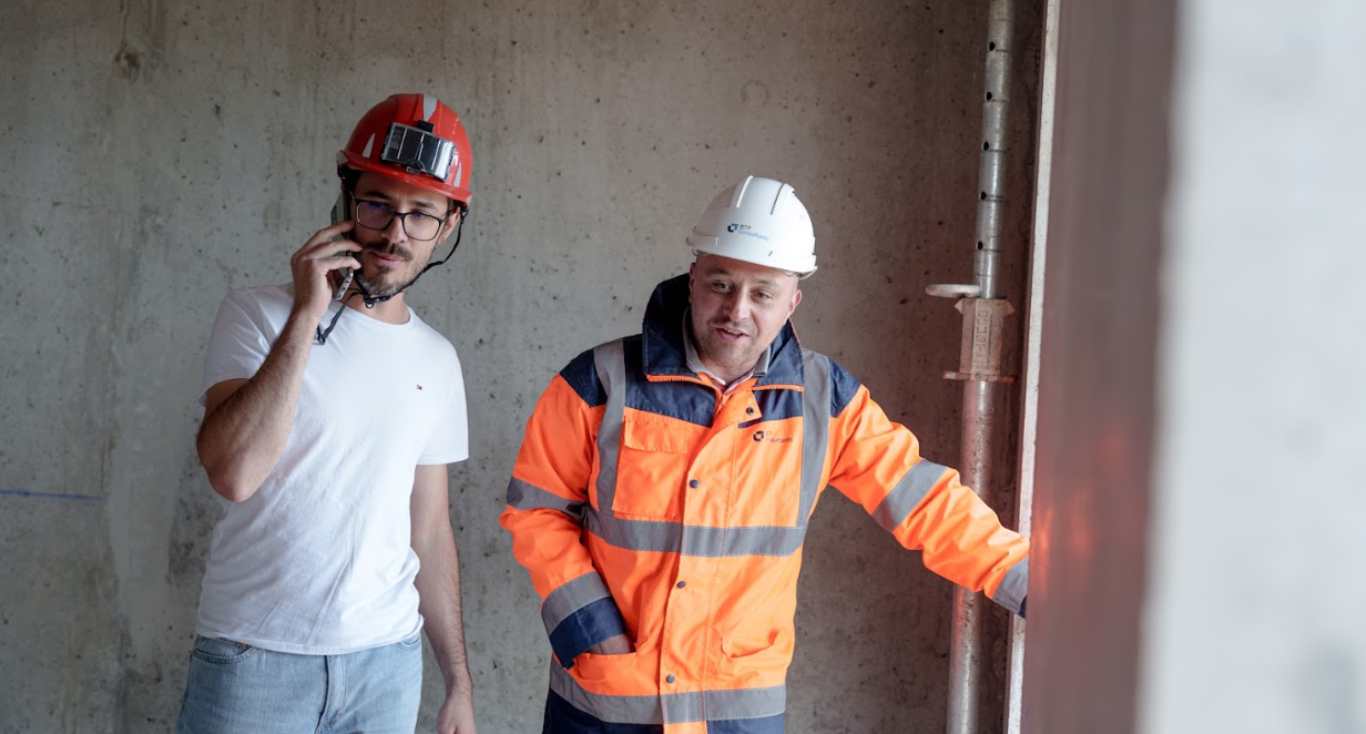 Deux techniciens en visite de chantier, l’un en EPI orange et casque, l’autre en discussion téléphonique